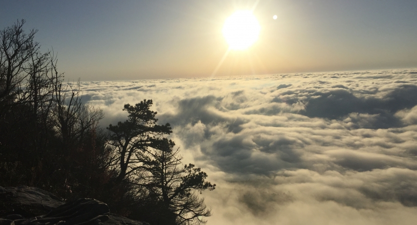 From a high elevation, clouds hide the ground as the sun rises above them